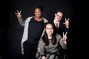Image of three students smiling and holding up hand with ring finger and pinky finger closed